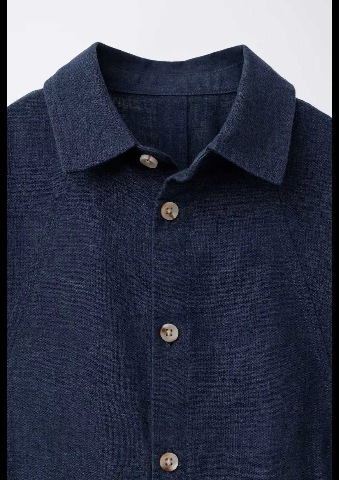 Close-up of navy linen shirt collar and natural shell buttons showing fabric texture and fine stitching detail