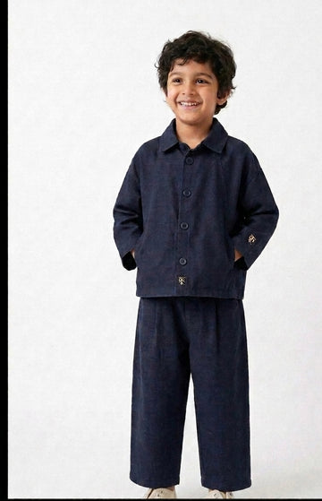 Boy wearing navy linen co-ord set with button-up shirt and wide-leg trousers, smiling against white background